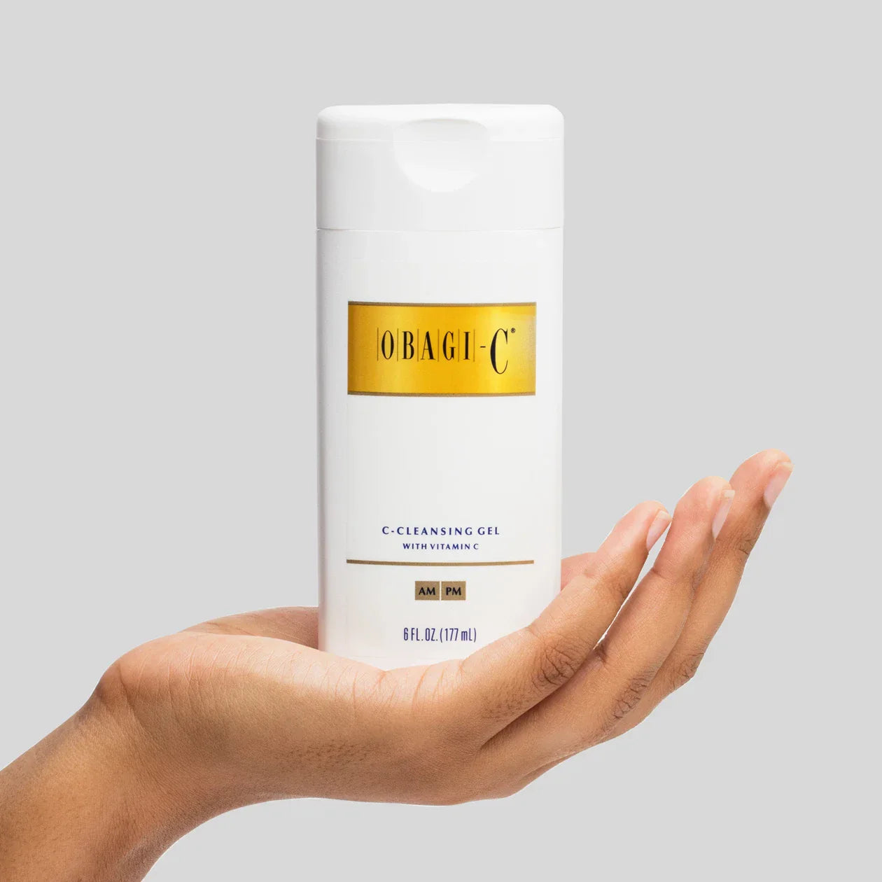 Obagi-C cleansing gel held in a hand against a gray background