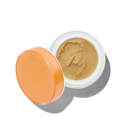 Open jar of beige cream with an orange lid on a white background